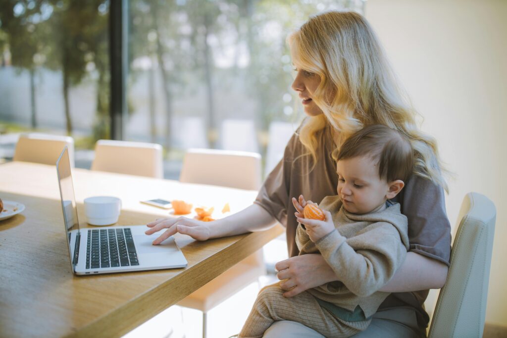 Frau mit Kleinkind auf dem Schoß sitzt am Laptop